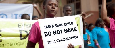 Young women holding sign, "I am a girl child, DO NOT MAKE me a child mother"