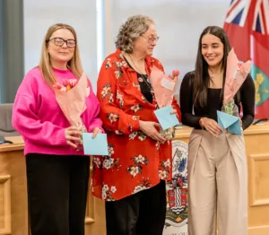 Three guest speakers hold bouquets and cards after presenting at International Women's Day event.