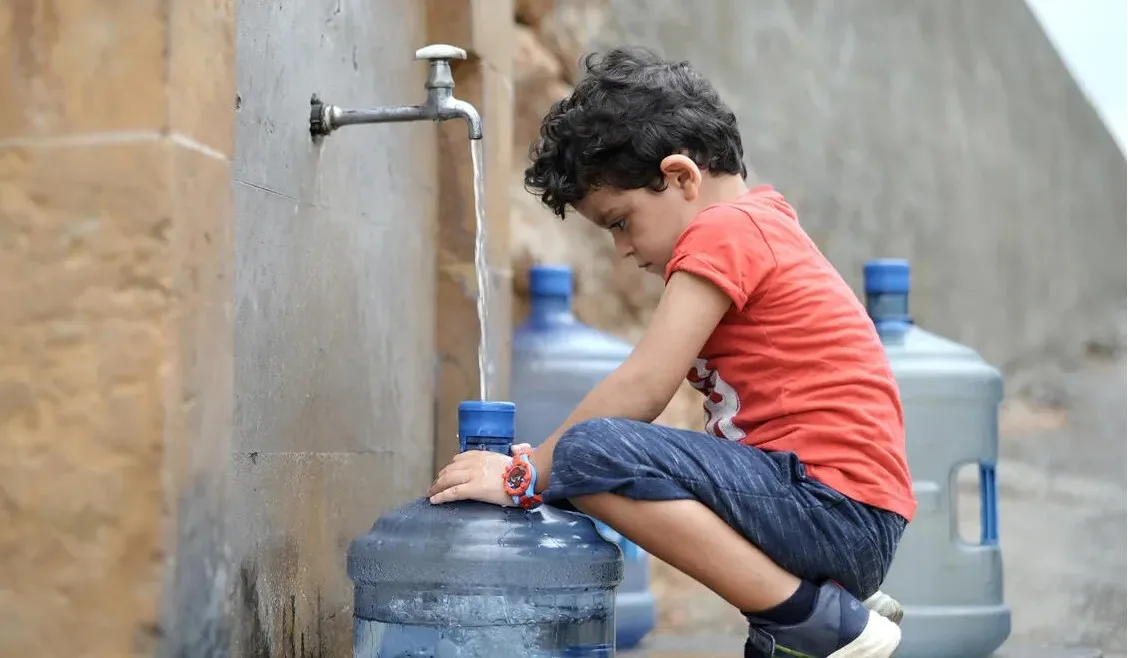 Small boy fills jug of water from a water tap.