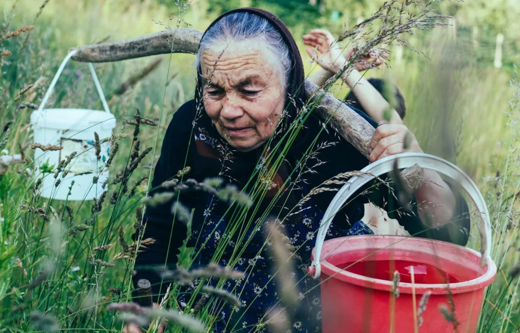 Older woman carrying two water pails on her shoulders