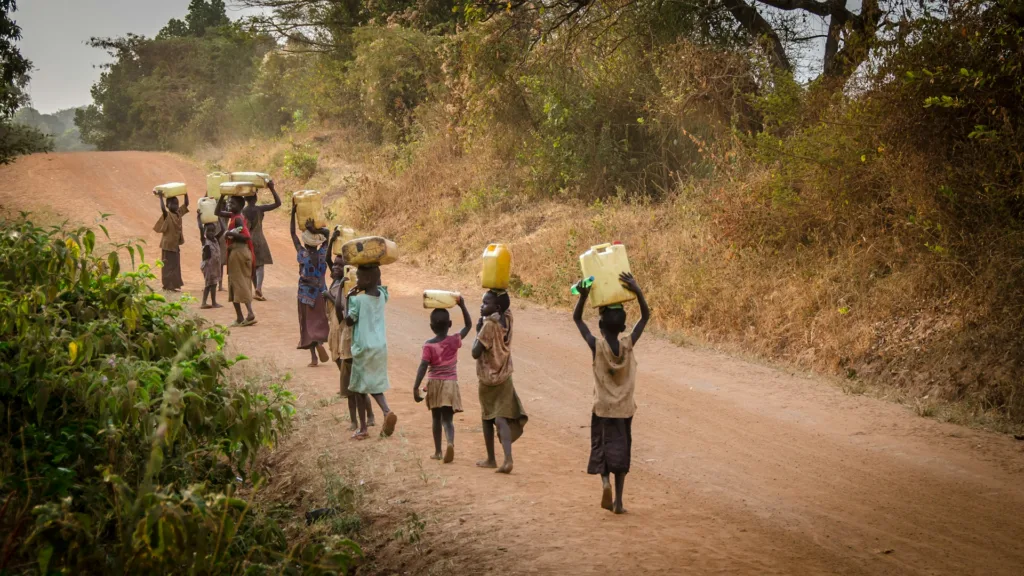 Women and children on rural road carrying water jugs on their heads