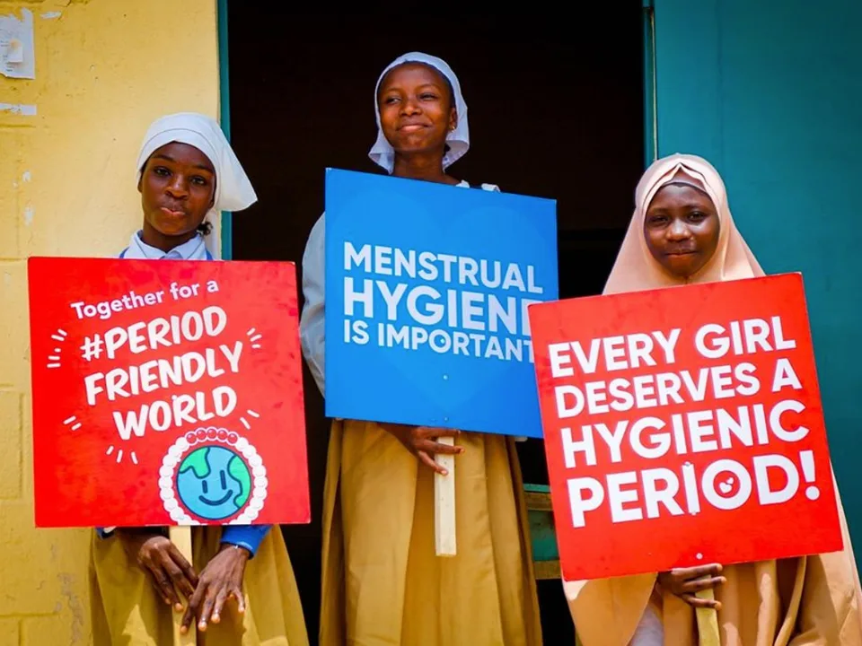 three girls hold up signs saying menstrual hygiene is important and every girl deserves a hygienic period and Together for a period-friendly world.